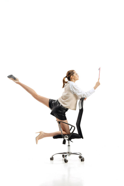 Portrait of young flexible woman in business style clothes with folder making twine isolated over white studio background - Φωτογραφία, εικόνα