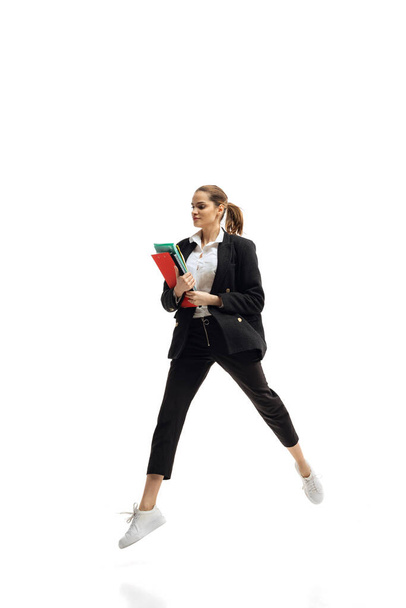 Dynamic portrait of young businesswoman in black suit holding folders, in motion isolated over white studio background - Photo, image