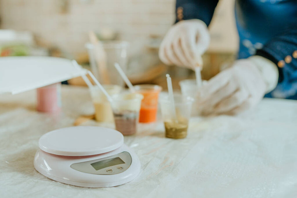 Artysta przygotowuje składniki do tworzenia zegara w technice sztuki żywicy. Kobieta w gumowych rękawiczkach dodająca płynne pigmenty do żywicy. Skupienie selektywne. - Zdjęcie, obraz