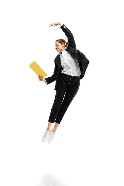 Dynamic portrait of young businesswoman in black suit jumping with folders isolated over white studio background. Ballet movements - Valokuva, kuva