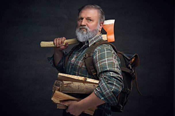 Ηλικιωμένος ξυλοκόπος με τσεκούρι και ξυλεία σε σκούρο φόντο - Φωτογραφία, εικόνα