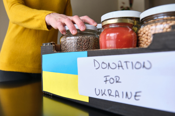 Nierozpoznana kobieta pakująca słoiki z jedzeniem do pudełka dla ukraińskich uchodźców - Zdjęcie, obraz
