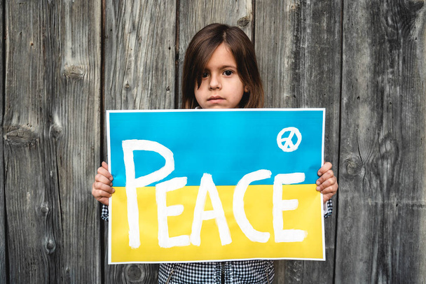 Portrait of the little girl with the Ukrainian flag placard and the inscription PEACE - Solidarity with Ukrainian children and people who are currently at war - Concept of war in Ukraine - Photo, Image