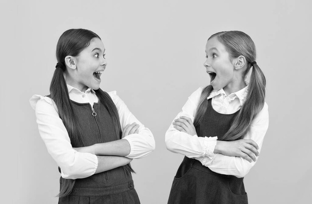 Crianças pequenas surpresas olham umas para as outras com bocas abertas em uniformes escolares formais, surpresa - Foto, Imagem