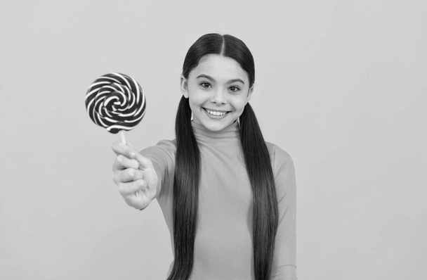 happy teen girl with lollipop candy on stick on yellow background, candy shop - Photo, Image