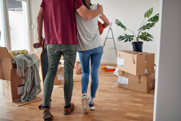 detail, cropped image of young male hugging his female partner in new apartment, holding skateboard, while she caring basketball - Fotografie, Obrázek