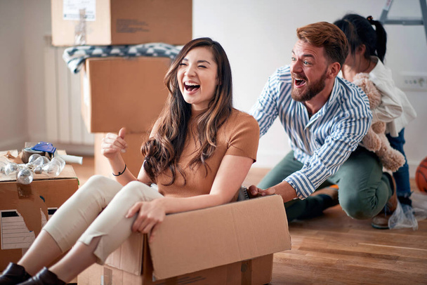 beautiful young asian young woman sitting in cardboard box, laughing, playing with her husband and daughter in new apartment. young family concept - 写真・画像