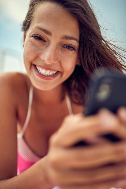 Close-up of a young sexy girl using a smartphone while posing for a photo and  enjoying a sunbath on a beautiful summer day. Summer, sea, vacation - Foto, Imagem