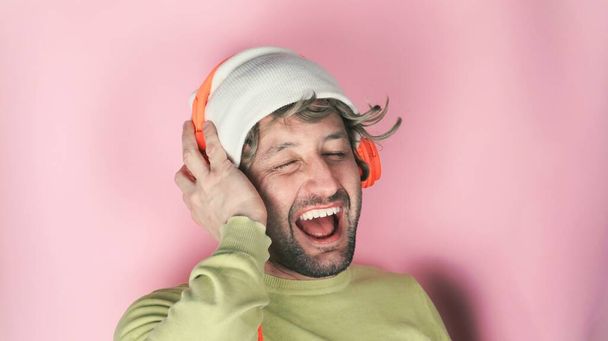 Young handsome man wearing headphones and listening to his favourite song, dancing, smiling with closed eyes - Фото, изображение