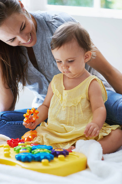 Teaching her little one. Shot of a cute baby girl sitting on the floor with her mom and playing with toys. - Photo, image