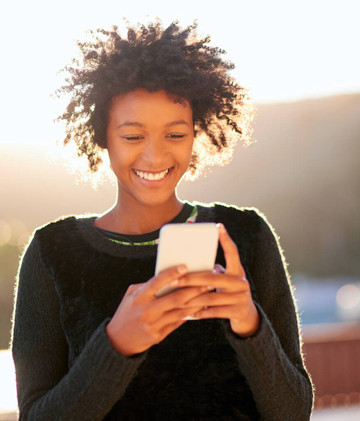 Aussenden von etwas Sonnenschein. Aufnahme einer attraktiven jungen Frau, die eine SMS sendet, während sie draußen spaziert. - Foto, Bild