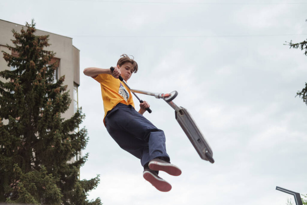 Zhytomyr, Ukraine - May 15, 2021: Teenager did unsuccessful trick on sportive push scooter on a city sports ground. He jumping over an obstacles. Extreme sports is popular among youth. Back rear view - Photo, image