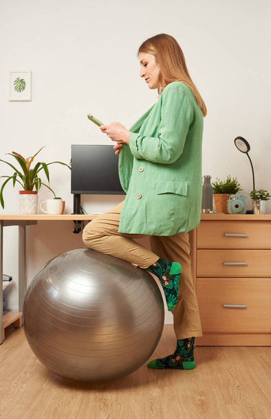 Mulher trabalhando em casa usa bola de fitness como uma cadeira - Foto, Imagem