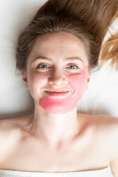 Alginische Maske auf dem Gesicht einer jungen Frau im Schönheitssalon. Kosmetische Behandlung, um die Haut jünger und frischer auf weißem Hintergrund zu machen - Foto, Bild