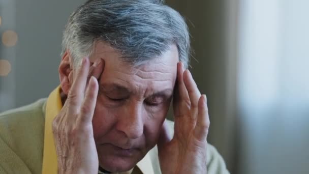 Detailní vyčerpaná frustrovaná tvář staršího muže dědeček masíruje nos most třít spánky trpí bolestí hlavy chronická migréna unavený nešťastný nezdravý kavkazský důchodce cítit vysoký krevní tlak - Záběry, video