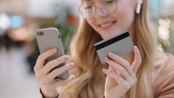 Κοντινό πλάνο χέρια νεαρή κοπέλα κρατώντας smartphone και πιστωτική κάρτα ευτυχισμένη γυναίκα πελάτη κάνουν online αγορά πληρώσει λογαριασμούς χρησιμοποιώντας τραπεζική εφαρμογή στο τηλέφωνο εικονική απομακρυσμένη ψώνια επιτυχημένη έννοια της ασφαλούς συναλλαγής - Πλάνα, βίντεο