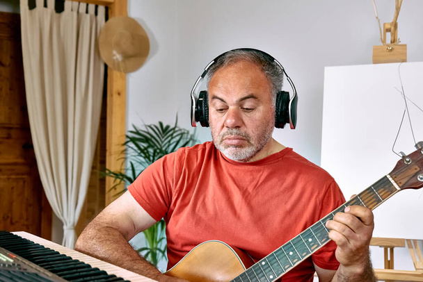 Пенсионер в наушниках играет на акустической гитаре и поет песни дома. Музыкальное хобби. Творческий досуг. Понятие самовыражения. - Фото, изображение
