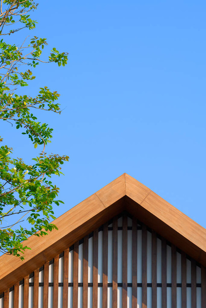 Lumière du soleil sur la surface du toit à pignon en bois vintage avec des branches d'arbre vert sur fond de ciel bleu clair dans un cadre vertical - Photo, image