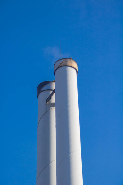 Schornsteine eines Holzpellet-Kraftwerks zur Nahwärmeversorgung vor blauem Himmel - Foto, Bild