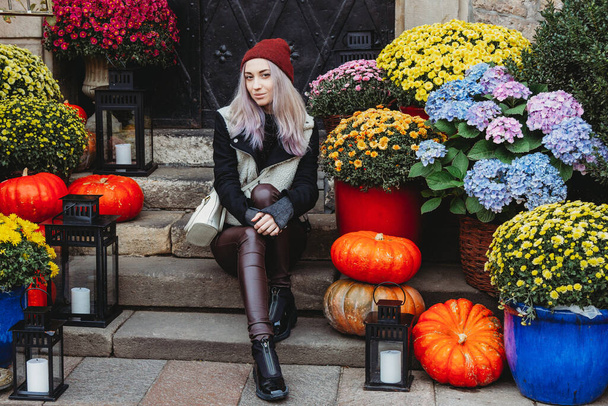 Beautiful young woman near the flower shop with autumn decoration on a street in a European city - Фото, зображення