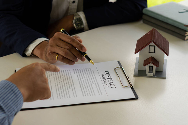 Der Makler verhandelt, bespricht die Bedingungen des Immobilienkaufvertrages und bittet den Kunden, einen Vertrag mit der Hausverwaltung, Vertragsunterlagen und Taschenrechner auf dem Tisch zu unterzeichnen.. - Foto, Bild