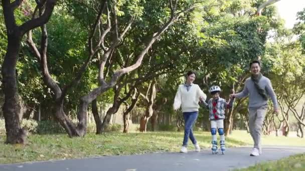 μικρό ασιατικό αγόρι μαθαίνουν πατινάζ σε εξωτερικούς χώρους στο πάρκο με τη βοήθεια από τους νέους γονείς - Πλάνα, βίντεο