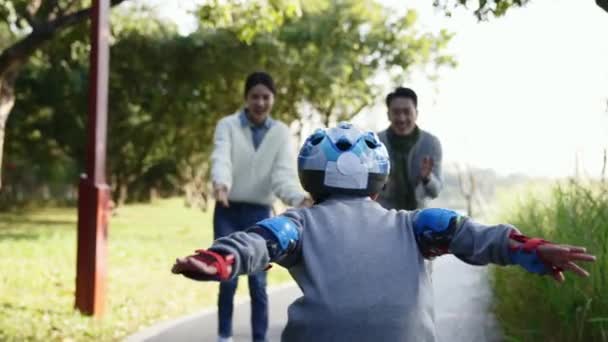 piccolo asiatico ragazzo apprendimento rullo pattinaggio all'aperto incoraggiato da genitori - Filmati, video