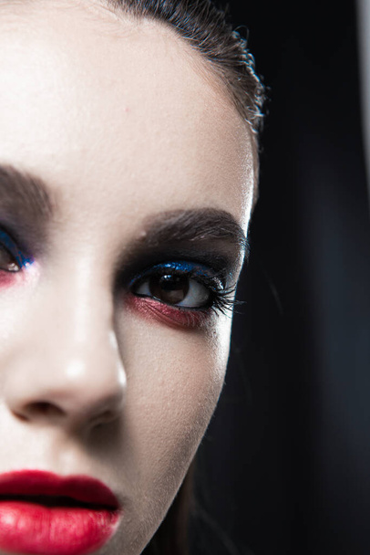 Retrato de beleza criativo com lábios vermelhos e olhos azuis em um fundo preto  - Foto, Imagem