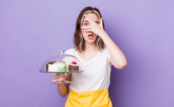 pretty caucasian woman looking shocked, scared or terrified, covering face with hand. home made cakes concept - Zdjęcie, obraz