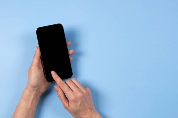 Női kéz megható okostelefon kijelző és mutató mutatóujjal üres mobiltelefon képernyőn világoskék háttér - Fotó, kép