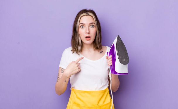 pretty caucasian woman looking shocked and surprised with mouth wide open, pointing to self. hand iron concept - Photo, image