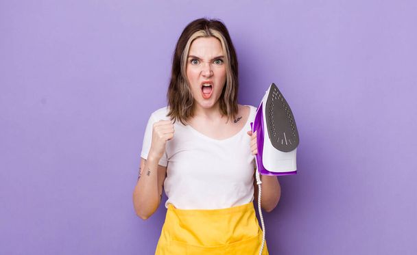 pretty caucasian woman shouting aggressively with an angry expression. hand iron concept - Fotoğraf, Görsel