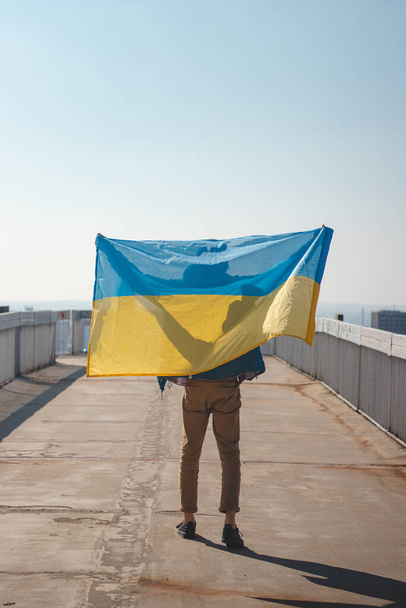 człowiek z ukraińską flagą przyłącza się do demonstracji wspierającej Ukrainę. Demonstracja przeciwko wojnie i okrucieństwom w XXI wieku. Wspieraj Ukrainę. Slava Ukraina.  - Zdjęcie, obraz