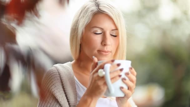 Beautiful, blonde young woman drinking tea in the garden - Felvétel, videó