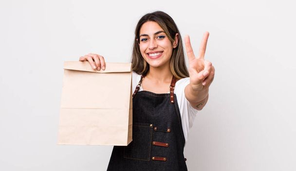 pretty hispanic woman smiling and looking friendly, showing number two. delivery and take away concept - Foto, afbeelding