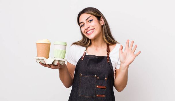 pretty hispanic woman smiling happily, waving hand, welcoming and greeting you. take away coffee concept - Фото, изображение