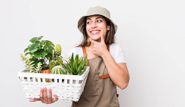 pretty hispanic woman smiling with a happy, confident expression with hand on chin. plants and gardering concept - Foto, imagen