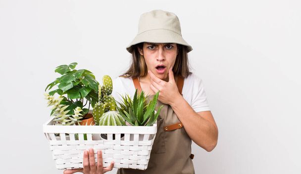 pretty hispanic woman with mouth and eyes wide open and hand on chin. plants and gardering concept - Photo, image