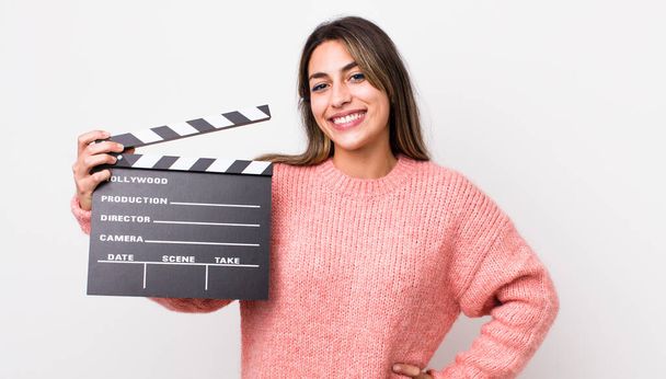 pretty hispanic woman smiling happily with a hand on hip and confident. cinema clapper concept - Фото, изображение