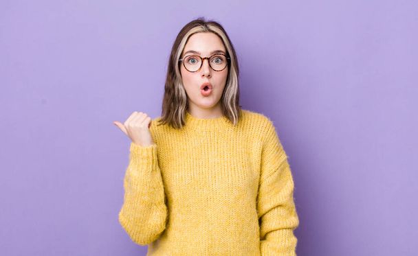 pretty caucasian woman looking astonished in disbelief, pointing at object on the side and saying wow, unbelievable - 写真・画像