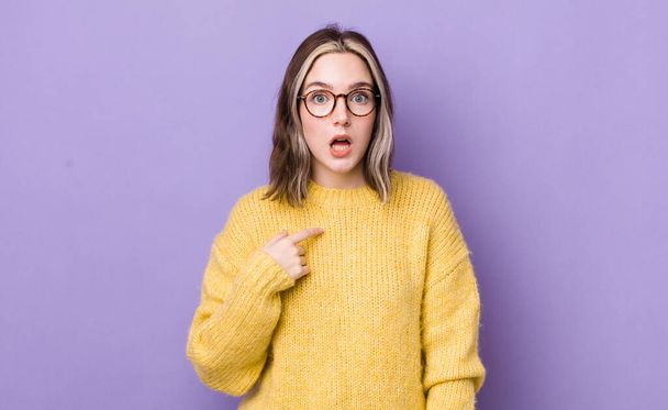 pretty caucasian woman looking shocked and surprised with mouth wide open, pointing to self - Foto, Bild