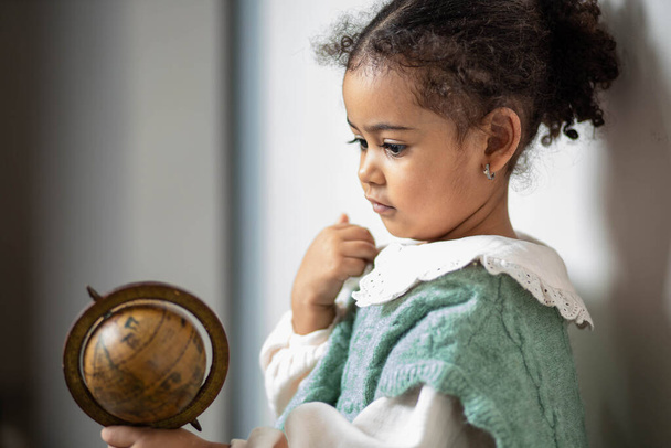 Little multiethnic girl looking at wooden Globus in her hands - Valokuva, kuva