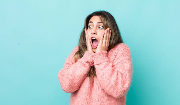 pretty hispanic woman feeling happy, excited and surprised, looking to the side with both hands on face - Фото, изображение