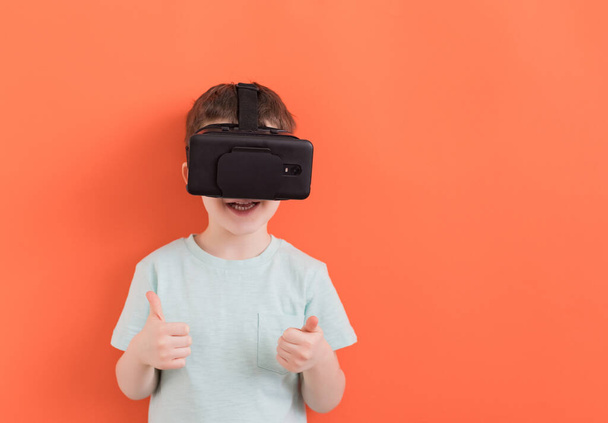 Caucasian child boy in virtual reality headset glasses on an orange background with copy space - Photo, Image