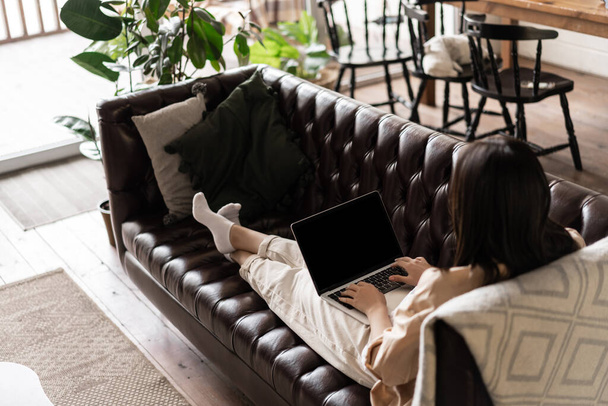 Takana näkymä nuori nainen rentouttava kotona kannettavan. Tyttö istuu sohvalla tietokoneen kanssa, katsella videoita tai selata sivustoja - Valokuva, kuva