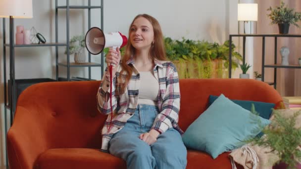 Junge Frau ruft in Megafon-Lautsprecher Rabatte beim Verkauf von Immobilien zu Hause auf dem Sofa an - Filmmaterial, Video