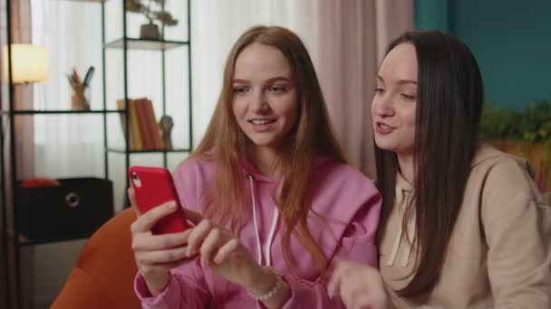 Веселі дівчата друзі і брати і сестри дивитися фотографії на смартфоні на дивані вдома, насолоджуватися соціальними медіа
 - Кадри, відео
