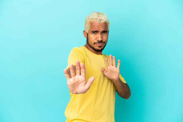 Молодой колумбийский красавчик на голубом фоне нервно протягивает руки к передней - Фото, изображение