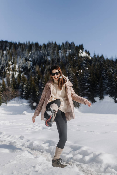 A girl in black glasses with a light jacket in full growth poses against the backdrop of snow-capped mountains. High quality photo - Photo, image