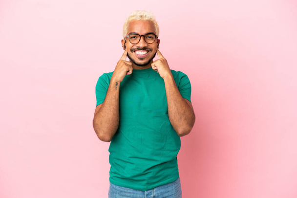 Young Colombian handsome man isolated on pink background smiling with a happy and pleasant expression - Fotografie, Obrázek